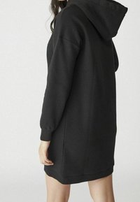 Abito felpa nero con cappuccio, maniche lunghe, polsini a coste e vestibilità comoda, realizzato in un morbido tessuto testurizzato.