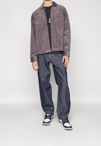 Chaqueta gris con cremallera y un patrón de cuadrícula, combinada con unos vaqueros oscuros de corte holgado y zapatillas negras y blancas. Diseño simple y casual.