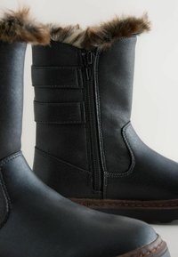 Zwarte winterlaarzen van glad synthetisch materiaal met een nep bont afwerking, een zijrits en drie banden voor stijl en verstelling.