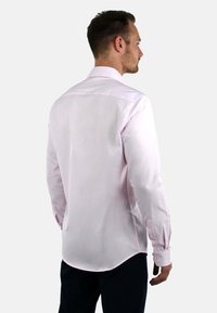 Lichtroze langemouwen shirt met een klassieke kraag, gladde textuur en een gebogen zoom, met knoopaccenten op de manchetten.