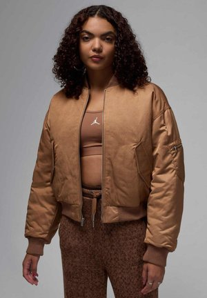 Giacca bomber marrone con zip sul davanti, polsini a costine e finitura satinata liscia. Indossata sopra un top marrone abbinato, che mostra un design minimalista.