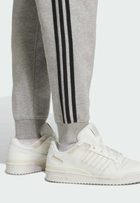 Grå sweatpants med sorte sidestrimler og tætsiddende manchetter, parret med hvide sneakers med en glat læderfinish og tre striber.