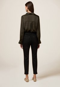 Olijfgroen satijnen shirt met een rugplooien, gecombineerd met zwarte aansluitende broeken, die goudkleurige hardware en een enkel-lange snit hebben.