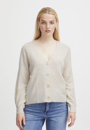 Beige V-Ausschnitt Strickjacke mit weicher Textur, drei Knöpfen auf der Vorderseite und gerippten Bündchen, kombiniert mit blauen Jeans.