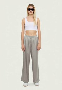 Pantaloni gri, largi, dintr-un material neted și ușor; asortați cu un top scurt alb și ochelari de soare; purtați cu încălțăminte albă.