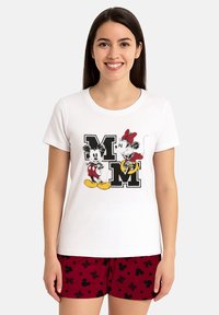 Donna che indossa una maglietta bianca con grafiche di Mickey e Minnie Mouse e pantaloni corti rossi con orecchie nere di Mickey e motivi a "M".