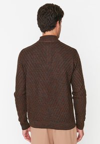 Braun-orange gemusterter Strickpullover mit Stehkragen und gerippten Bündchen, mit strukturierter Oberfläche und figurbetontem Schnitt.