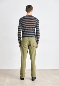 Stripet langermet skjorte i marineblå og beige, kombinert med olivenfargede bukser. Har en avslappet passform, basic rund hals, og minimal detaljering.