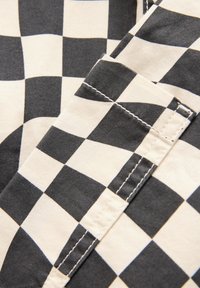 Gros plan sur un tissu à carreaux noir et blanc avec des coutures superposées cousues et un détail de couture visible.