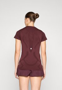 Maron atletisk skjorte med en tætsiddende design, korte ærmer og prægede mønster på ryggen. Sammen med matchende shorts.