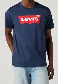 Námořnická modrá bavlněná tričko s výrazným červeným logem Levi's přes hrudník, krátké rukávy a klasický kulatý výstřih.