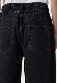 Pantaloni in denim nero con vita elasticizzata arricciata, due tasche posteriori e vestibilità rilassata. Il tessuto è morbido al tatto e leggermente elasticizzato.