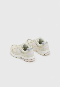 Beige athletic shoes with mesh and leather upper, soft gray accents, rounded toe, and textured sole featuring light pink details.
