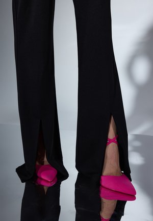 Mustat housut sivuhalkioilla, joissa kirkkaan pinkit, kärjestä terävät kengät ristikkäisillä nilkkahihnoilla. Sileä, kiiltävä kangaspinta.