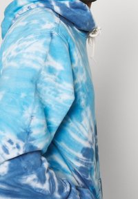 Felpa con cappuccio tie-dye azzurro chiaro realizzata in tessuto morbido, caratterizzata da un cappuccio con cordini e una vestibilità comoda, con motivi che presentano diverse sfumature di blu e bianco.