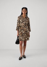 Rochie cu imprimeu de leopard, cu guler, curea și mâneci trei sferturi. Confecționată dintr-un material neted. Geanta neagră și pantofii comozi completează ținuta.