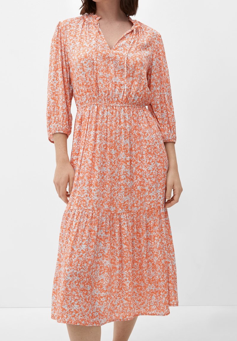 Kwiecista sukienka midi w pomarańczowo-białym kolorze, z dekoltem w kształcie litery V, wykończona rękawami do łokcia, elastycznym pasem oraz warstwowym dołem. Wykonana z miękkiej tkaniny. 