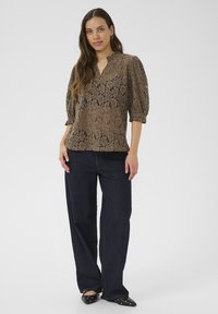 Brun blondeløs bluse med puffede ærmer, v-hals, parret med mørkeblå vidde ben jeans og sorte spidse hæle med sølvnitter.