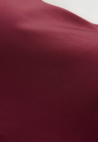 Tela burdeos con una superficie lisa y ligeramente texturizada que muestra un patrón de costillas diagonales. La luz se refleja sutilmente, resaltando la profundidad del material.