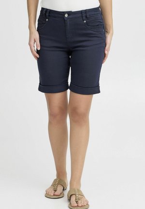 Bermudas en denim navy avec ourlets retroussés, design cinq poches et fermeture à bouton devant. Portées avec des sandales beige, à semelle plate, et accents décoratifs.