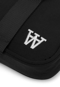 Sac en tissu noir avec une surface texturée, présentant un logo blanc brodé. Comprend une sangle noire solide pour le transport.