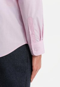 Camisa de manga larga rosa claro con puños abotonados, que presenta una textura suave y un ligero brillo, combinada con pantalones oscuros de textura.