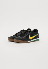 Černé atletické boty s texturovaným povrchem, zdobené žlutým logem Nike, zelenými akcenty a gumovou podrážkou.