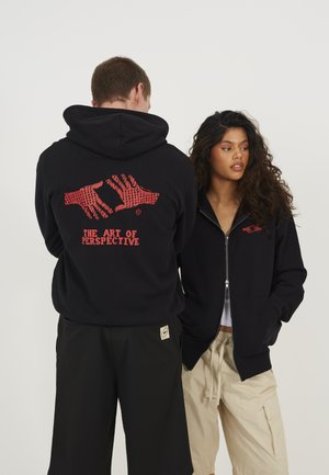Black hooded sweatshirt featuring red graphic design. The back shows hand illustrations with "THE ART OF PERSPECTIVE" text. Soft fabric.