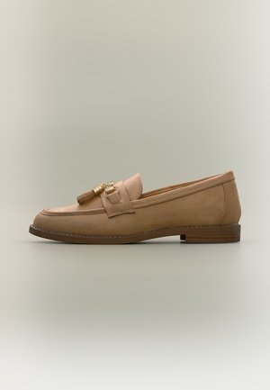 Mocassin en daim marron clair avec petit talon, pompons décoratifs et accents dorés sur un fond uni.