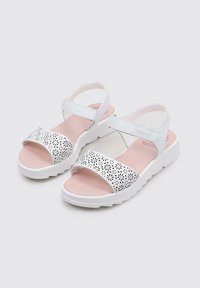 Sandalias blancas con patrón floral perforado en la tira, plantilla acolchada rosa, correa ajustable en el tobillo y suela blanca gruesa.