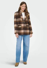 Blazer de cuadros marrón y beige con cuello de muesca, dos bolsillos frontales y botones negros, combinado con jeans de pierna ancha azul claro.