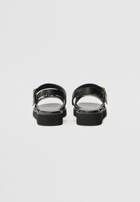 Schwarze Sandalen mit zwei verstellbaren Riemen, glatter Oberfläche, dicken Gummisohlen und einem metallischen Schnallenakzent.