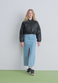 Melnā īsā bomber jakā, gaiši zila džinsa svārku ar priekšējo izgriezumu, melni sporta apavi un baltas zeķes, uz modeļa uz vienkārša fona.