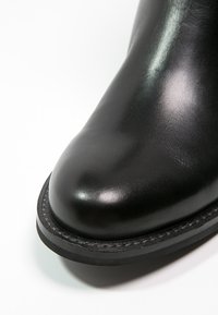Black leather ankle boot with a smooth texture, rounded toe, and durable rubber sole, featuring a subtle stitched accent around the edge.