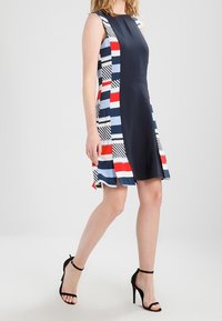Vestido navy con paneles laterales en rojo, blanco y azul a rayas, con diseño sin mangas y falda a la altura de la rodilla. Combinado con tacones negros.