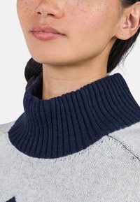 Marineblau gerippter Rollkragen, kombiniert mit einem hellgrauenSweater-Oberteil, das eine weiche Strickstruktur und kontrastierende Farben zeigt.