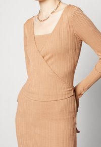 Top moulant et côtelé dans une teinte beige chaude, doté d'un décolleté carré et de manches longues. Le tissu paraît doux avec un léger brillant.