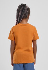 T-shirt arancione in cotone a maniche corte con collo a girocollo, texture liscia e un piccolo dettaglio con etichetta sul lato vicino all'orlo.