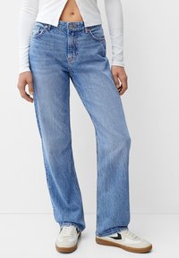 Lichtblauwe high-waisted denim jeans met een recht gesneden design, vijf zakken en subtiele stikdetails. Draag met witte sneakers.