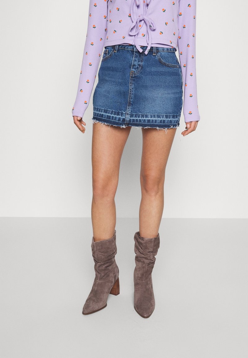 Jeans mini kjol med fransar i nederkant, tillsammans med en lila långärmad topp med blommönster och grå slouchiga klackskor.