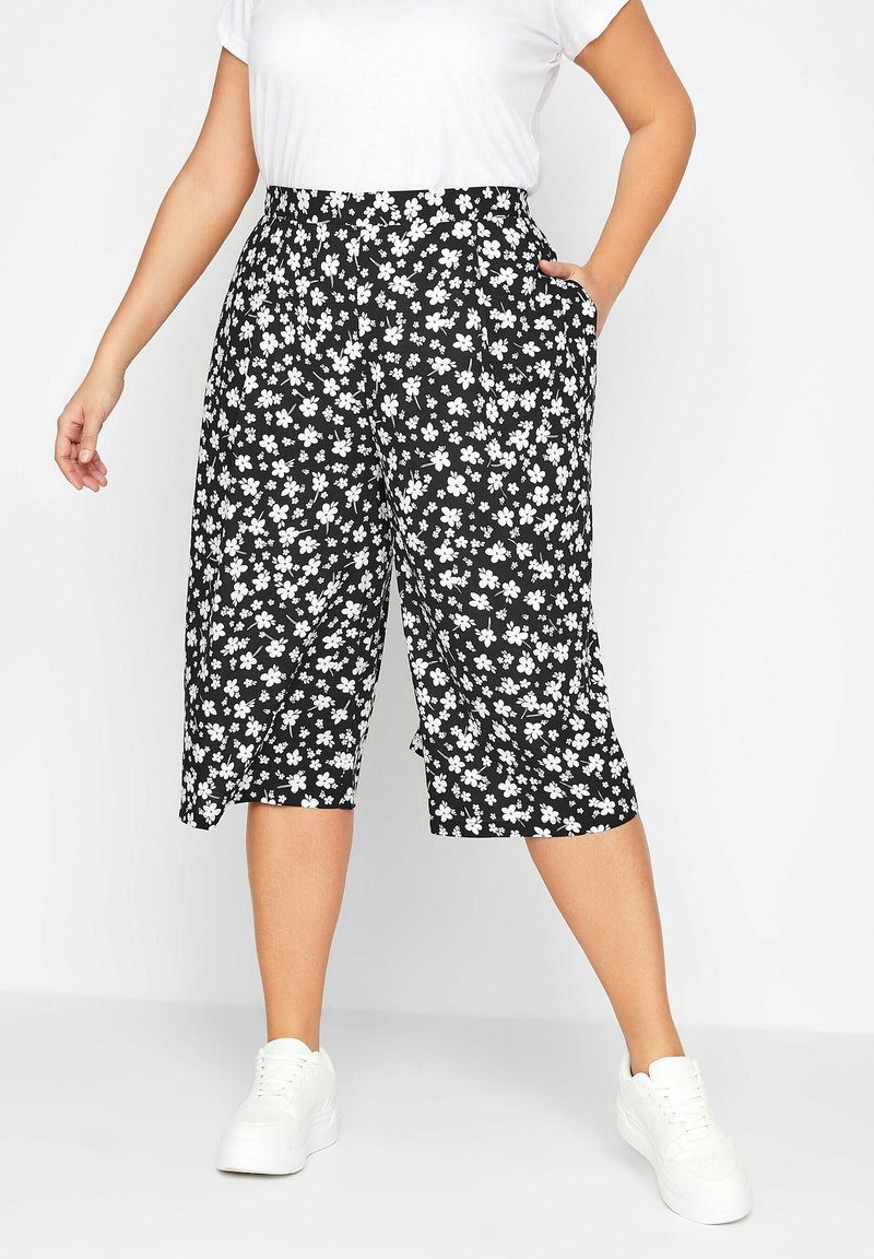 Černé kalhoty culottes s bílým květinovým potiskem, vysokým pasem a postranními kapsami. Nosené s bílým tričkem a kombinované s bílými teniskami.