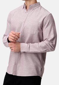 Chemise boutonnée en tissu mauve clair, à manches longues, avec une poche poitrine unique et une texture lisse avec un motif subtil.