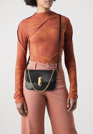 Schwarze Leder-Crossbody-Tasche mit vernickelter Hardware, Kettenriemen und Klappenverschluss. Begleitet von einem passenden orangefarbenen Langarmoberteil.
