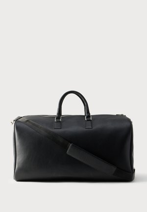 Schwarze Leder-Reisetasche mit zwei Griffen und einem verstellbaren Schultergurt vor einfarbigem Hintergrund.