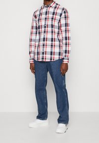 Rood, marineblauw en witte geruite overhemden met lange mouwen en een kraag, gecombineerd met blauwe jeans en witte sneakers.