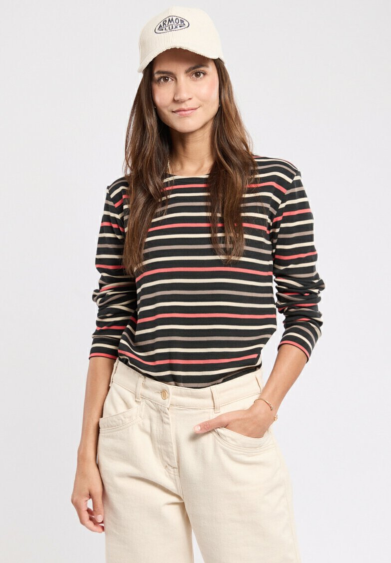 Schwarzes Langarmshirt mit horizontalen roten und cremefarbenen Streifen, kombiniert mit cremefarbenen, hochtaillierten Hosen und einer beigefarbenen Kappe mit einem Logo.