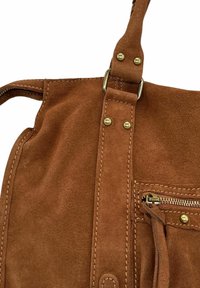 Sac à main en daim marron avec une bandoulière fixée par des rivets dorés, poche zippée visible et coutures détaillées sur un fond blanc.