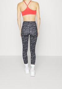 Czerony stanik sportowy z wycięciem na plecach, w połączeniu z czarnymi legginsami o wysokim stanie w leopardzi wzór. Białe buty sportowe.