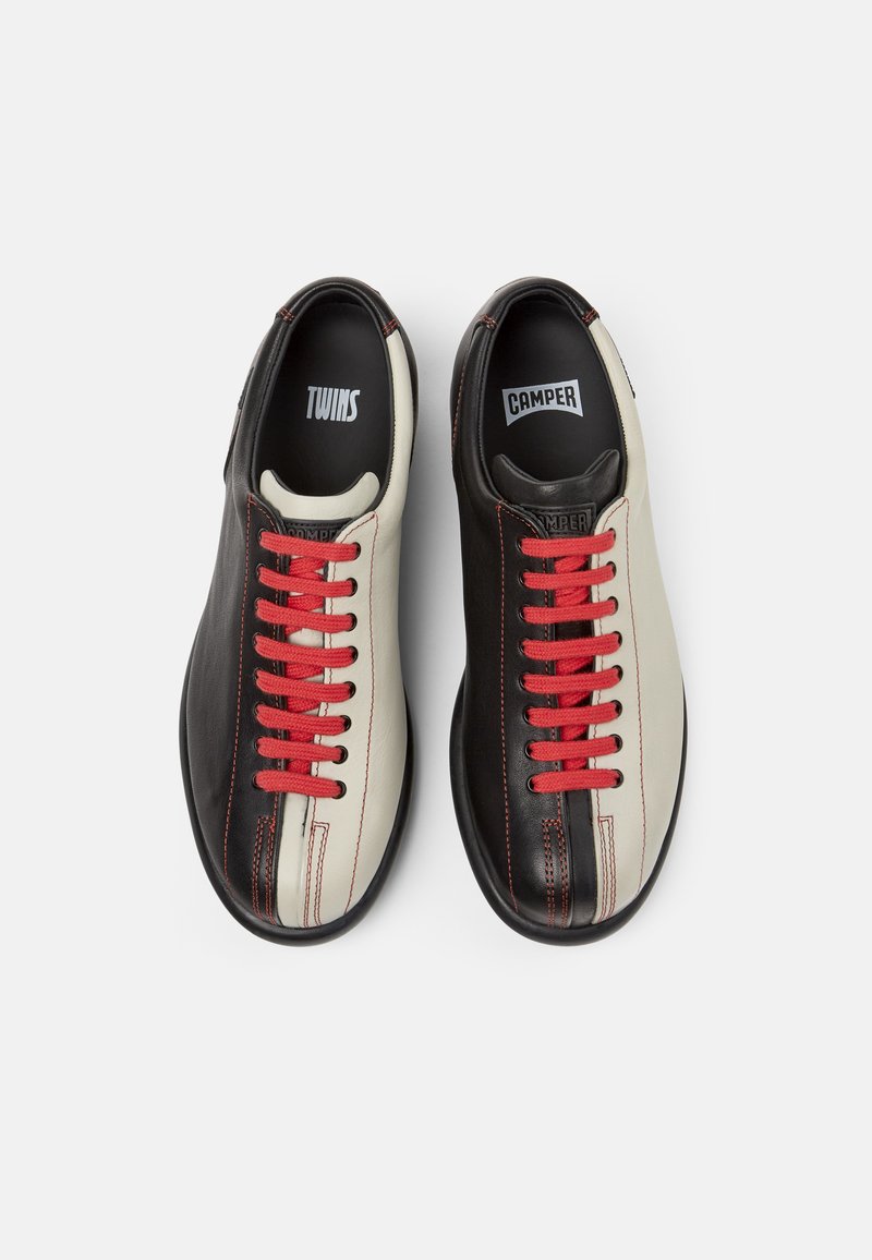 Zapatos de cuero negros y crema con cordones y costuras rojas, con punta redondeada y diseño de paneles de colores contrastantes. Nombres de marcas en el interior.