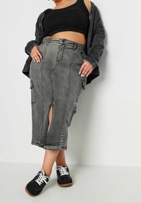 Grå denim midi-kjol med framtida slits, cargofickor och en figurnära design. Matchad med en svart crop top och svarta sneakers.